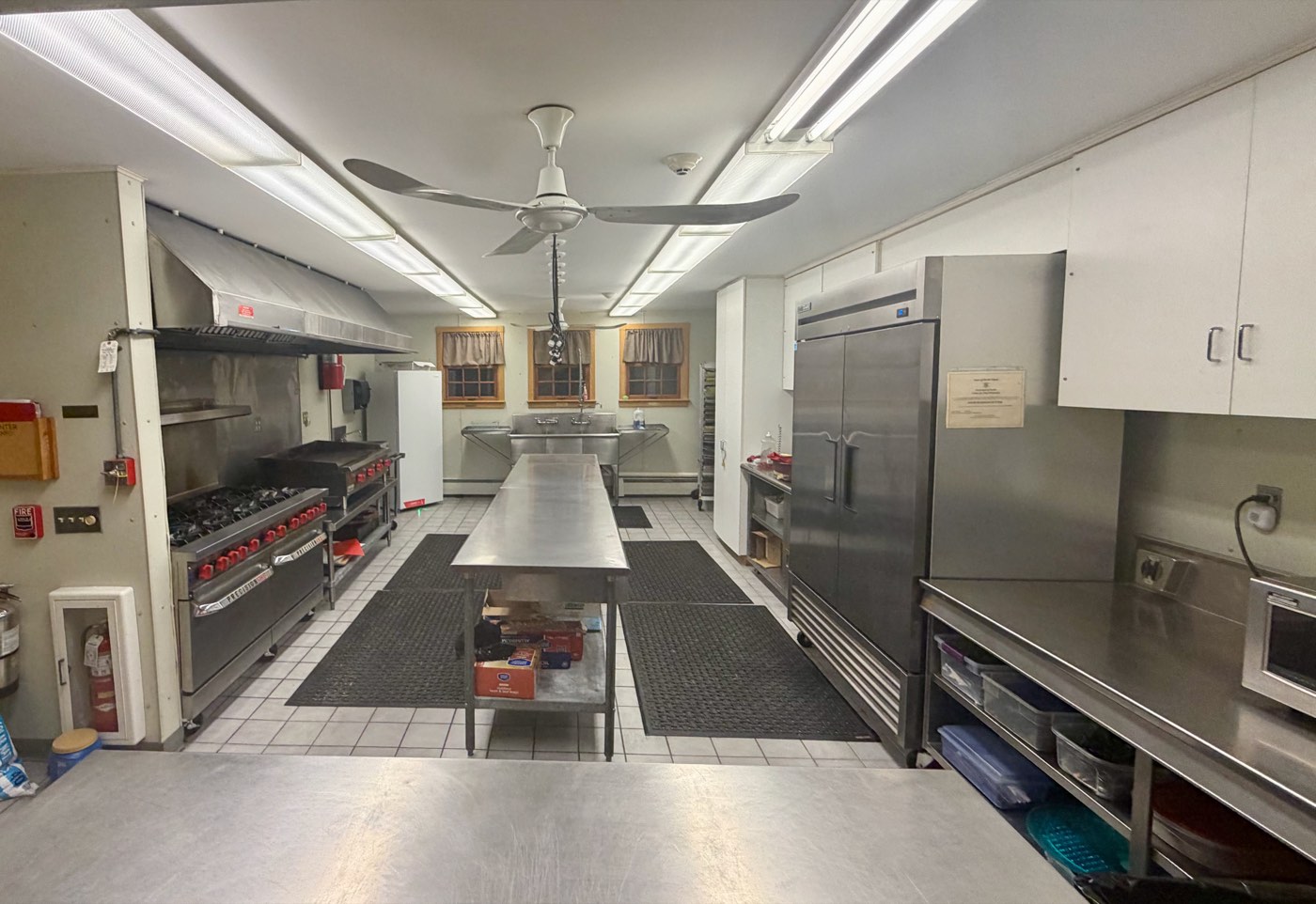 The commercial kitchen, with a range, griddle, prep table, and reach-in refrigeration.